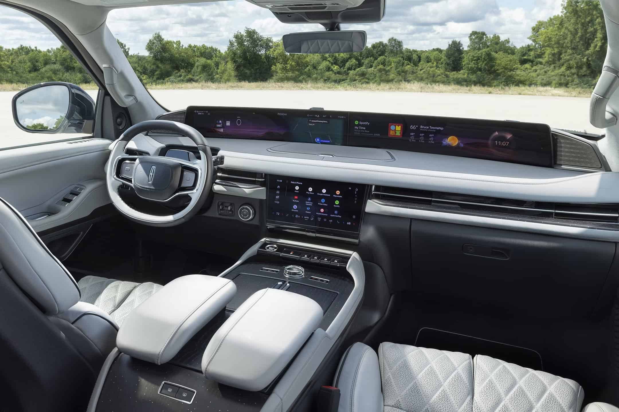 Interior wide-angle view of a Lincoln Nautilus featuring a "Light Space" color scheme with light gray quilted leather seats and a white-rimmed steering wheel. The massive 48-inch panoramic display is active, showing navigation and media widgets against a bright, daylight exterior background.